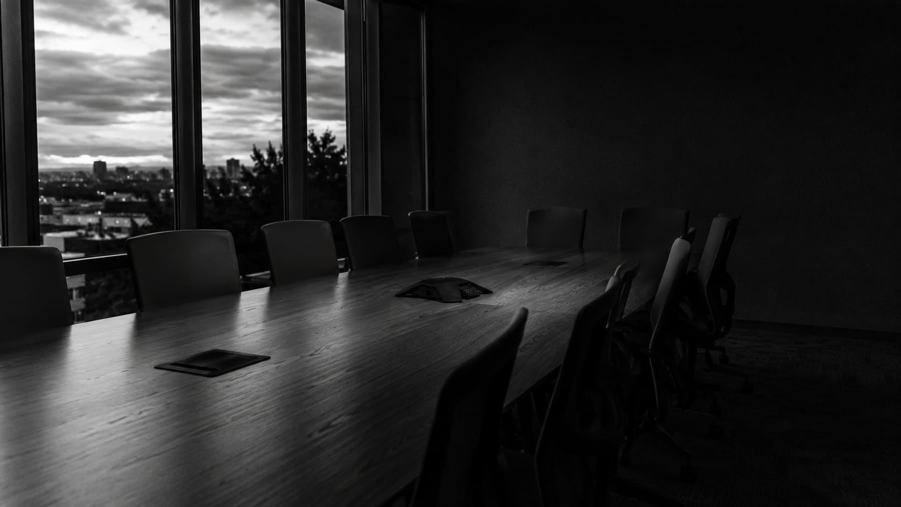 Sala de reuniones vacía al anochecer, con la mesa del consejo iluminada por la luz del ventanal